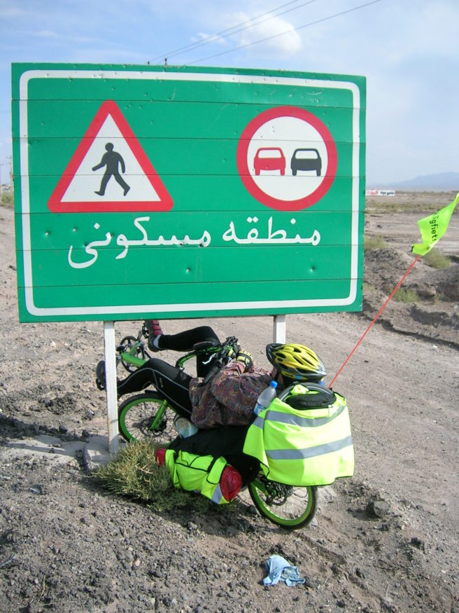 Ligfietser onder een bord op een zandweg