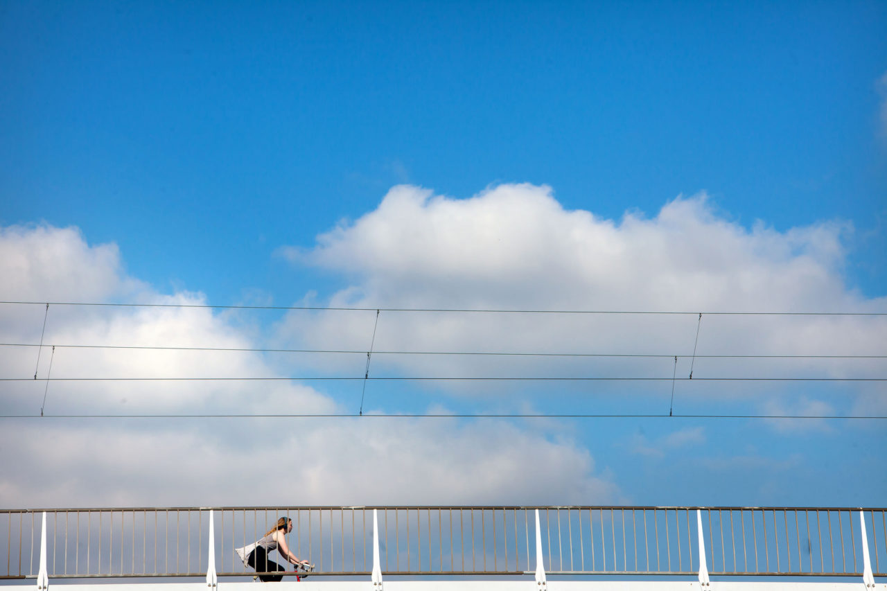 Vrouw fietst op brug in Rotterdam met wolken